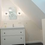 Badezimmer mit Waschbecken, Spiegel und Heizung unter schräger Decke.