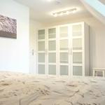 Schlafzimmer mit Dachschräge, weißer Kleiderschrank und Bett mit Musterdecke.