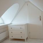 Schlafzimmer mit Dachschrägen, Fenster und weißen Möbeln.