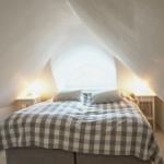 Schlafzimmer mit Dachschrägen, Bett mit kariertem Bettbezug und Fenster