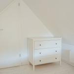 Zimmer mit weißen Wänden, Schrank und Tür unter Dachschrägen.