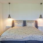 Schlafzimmer mit Bett, zwei Nachttischen und Hängelampen. Fenster mit Vorhängen.