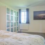 Schlafzimmer mit Bett, Kleiderschrank und Fenster. Wandbild und kleiner Hocker.