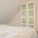 Schlafzimmer mit Dachschräge, weiße Schrankwand und Blick auf Treppe.