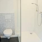 Badezimmer mit Dusche und WC. Wand mit Blumenmotiv. Fliesen und Spiegel.