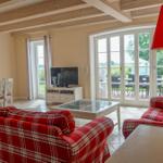 Wohn- und Essbereich mit rotem Plaid-Sofa, TV und Blick auf Terrasse.