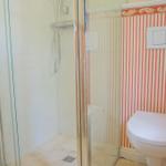 Bad mit Dusche und WC, Wand mit roten Streifen und weißem WC.
