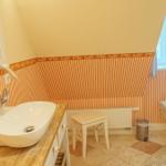 Badezimmer mit Waschbecken, Toilette und Fenster. Wandverkleidung mit Streifenmuster.