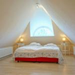 Schlafzimmer mit Dachschrägen, Bett mit floraler Bettwäsche und runden Fenstern.
