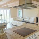 Küche mit Steinarbeitsplatte, Essbereich und Wohnzimmer mit weißen Sofas und Holzdecke.