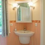 Badezimmer mit Waschbecken, Spiegel und Fenster mit Blick auf Grün.