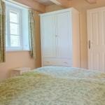 Schlafzimmer mit Bett, Kleiderschrank und Fenster. Tür führt in ein weiteres Zimmer.