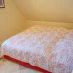 Schlafzimmer mit Dachschräge, Bett mit rosa-weißem Muster und Fenster mit Vorhängen.