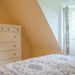 Schlafzimmer mit Dachschrägen, weißer Kommode und Bett mit floraler Bettwäsche.
