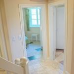 Hausflur mit Treppe, Tür zu Schlafzimmer und Bad. Fliesenboden und Fenster mit Vorhang.