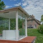 Glasstruktur mit Whirlpool und Dusche im Freien. Hintergrund: traditionelles Haus mit Schieferdach.