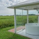 Eine runde Whirlpool-Badewanne in einer Glasveranda mit Blick auf eine grüne Landschaft.