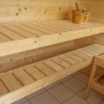 Sauna mit Holzbank und Steinofen. Holzgehäuse und Körbe sind sichtbar.