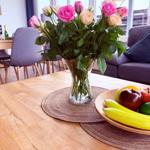 Holztisch mit Blumen und Obst, Sitzgelegenheiten im Hintergrund