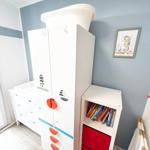 Kinderzimmer mit weißem Schrank, Bücherregal und Wandbild mit Seeoste.