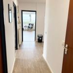 Flur mit Holzdielen führt in Wohnzimmer mit Sitzgelegenheit und Fenster.