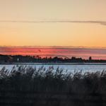 Sonnenuntergang über dem Wasser mit Seglern und einer Brücke im Hintergrund.