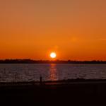 Sonnenuntergang über Wasser mit Windrad am Horizont.