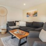 Wohnzimmer mit grauem Sofa, Holztisch und Wandbild