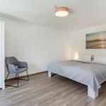 Schlafzimmer mit Bett, Schreibtischstuhl und Kleiderschrank. Wandbild zeigt Strand.