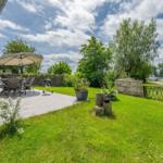 Terrasse mit Tisch, Stühlen und Grill. Grünfläche, Zaun und Bootsanlegestelle im Hintergrund.