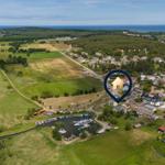 Aerielansicht eines Dorfes mit Seeufer, Bootshafen und Wald. Ein markanter Standortpunkt ist hervorgehoben.