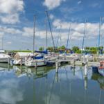 Mehrere Segelboote und Motorboote liegen im Hafen. Der Himmel ist blau mit weißen Wolken.