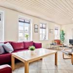 Wohnzimmer mit rotem Sofa, Holztisch und Sessel. Mehrere Fenster und helle Wände.