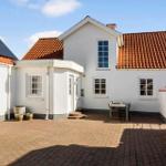 Weiße Villa mit rotem Dach und gepflastertem Hof. Tisch und Stühle stehen im Freien.
