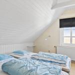 Schlafzimmer mit Dachschrägen, Bett mit blauen Kissen und Decke, Fenster mit Jalousie.