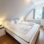 Schlafzimmer mit Doppelbett, Nachttisch und Fenster mit Vorhängen.