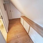 Schlafzimmer mit Holzboden und Schrank unter Dachschräge. Toilettenbereich ist angrenzend.