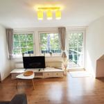 Wohnzimmer mit Holzboden, Fernseher und Fenstern zum Balkon.