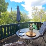 Terrasse mit Tisch, Stuhl und Sonnenschirm. Blick auf grüne Bäume und einen Kirchturm.