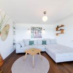 Wohnzimmer mit grauem Sofa, Holztisch und großer Vase.