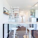 Moderne Küche mit Esstisch, weißen Barhockern und einer Treppe.