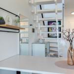 Helle Wohnung mit Treppe, Tisch und Wandregal mit Pflanzen und Uhr.