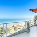 Terrasse mit Blick auf das Meer und Strand. Orange Markise, grüne Stühle und Pflanze.