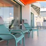 Terrasse mit zwei mintgrünen Liegestühlen, orangefarbenem Markisenüberdachung und Pflanze.