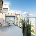 Terrasse mit zwei Liegestühlen und Meerblick. Hintergrund: Strand und blaues Wasser.