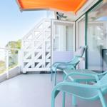 Terrasse mit zwei hellblauen Stühlen und orangefarbenem Sonnenschutz. Blick auf den Himmel und die Umgebung.