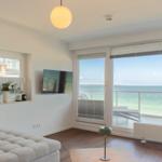 Wohnzimmer mit Meerblick, TV und Balkon. Holzboden und weiß gestrichene Wände.