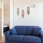 Blauer Sofa im Wohnbereich mit drei Surfboard-Decorations an der Wand. Durchgang zur Schlafzimmer.