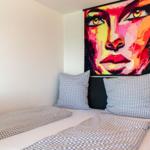 Ein Bett mit karierten Kissen und Decke, an der Wand hängt ein großes Porträt.