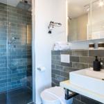 Badezimmer mit Dusche, Waschbecken und Toilette. Fliesenwand und Spiegel sichtbar.